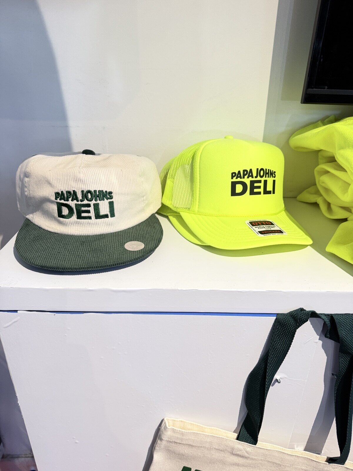 Two custom-branded caps displayed on a white shelf beside folded neon yellow apparel